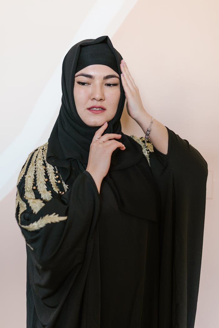 Elegant portrait of a woman in a traditional black hijab and long-sleeved dress with hand on chin.