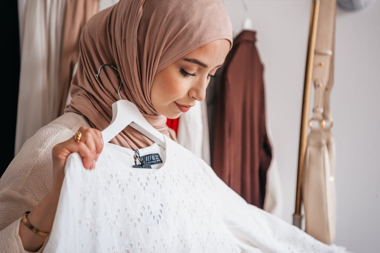 A woman in a hijab examines a stylish outfit in an indoor setting, showcasing modern Islamic fashion.